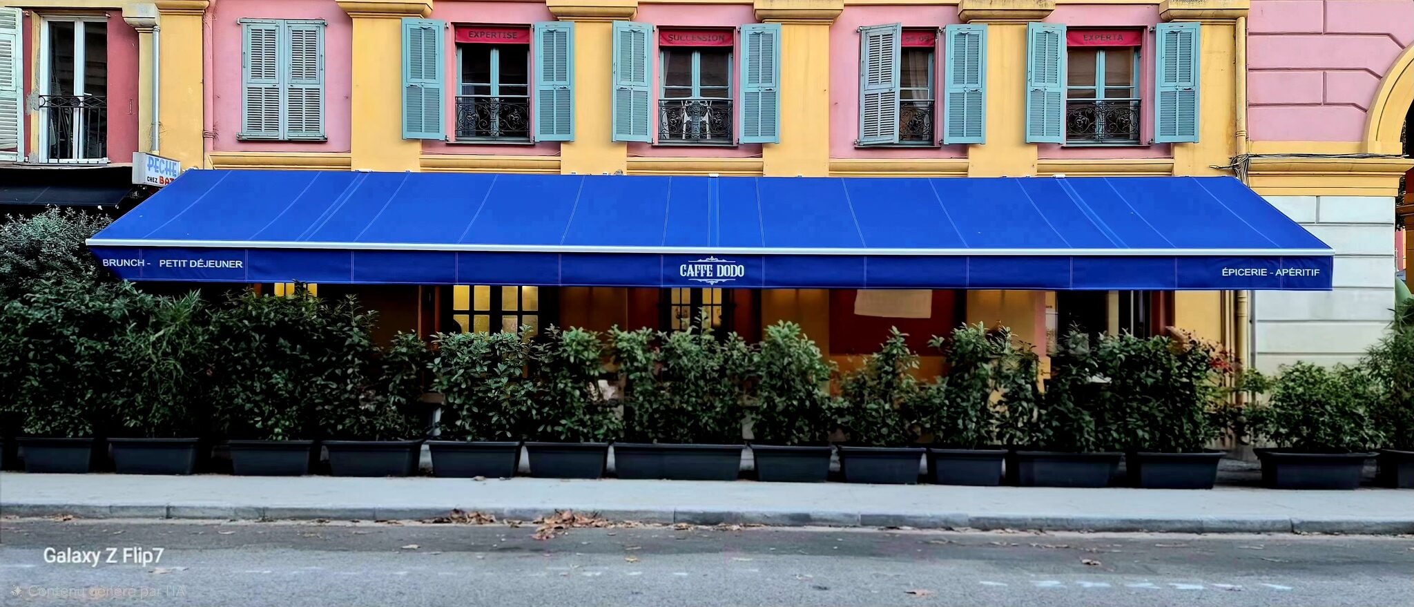 Bâtiment jaune-rose, volets turquoise, enseigne du Café Dodo, plantes en pot sur le trottoir.