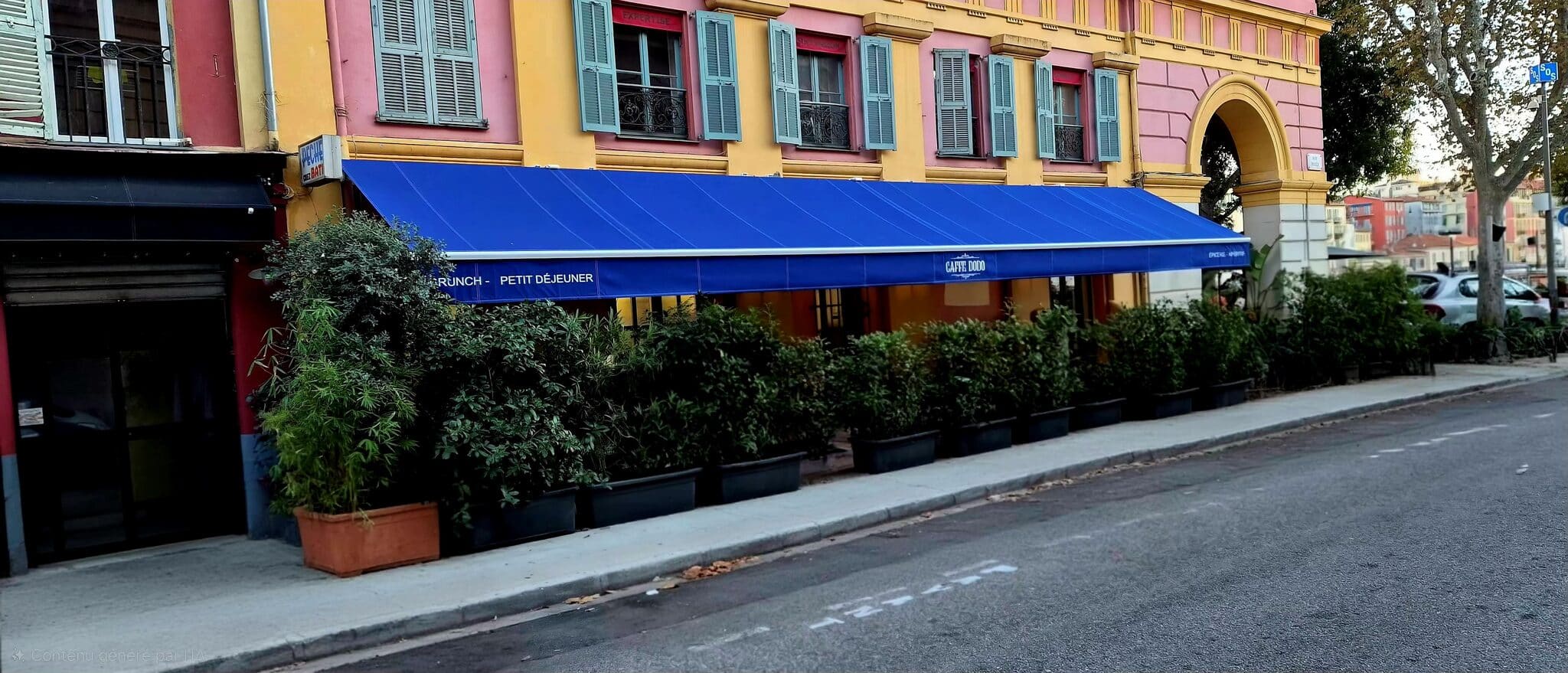 Bâtiment coloré, auvent bleu, plantes en pot, fenêtres à volets au-dessus.