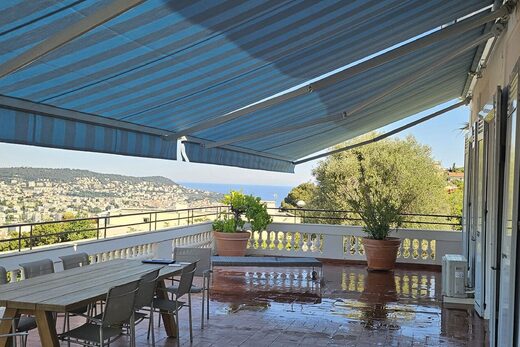 Terrasse villa Pessicart, vue Nice, store bleu, meubles bois.
