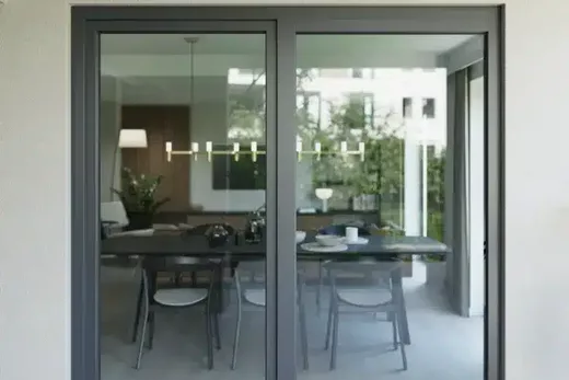 La porte coulissante en verre montre une salle à manger moderne avec une table, des chaises et une atmosphère élégante inspirée de Brouillon.