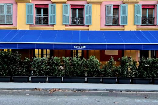 Bâtiment jaune-rose, volets turquoise, enseigne du Café Dodo, plantes en pot sur le trottoir.